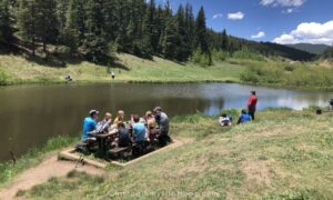 people at a picnic table by a lake enjoying the best hiking snacks