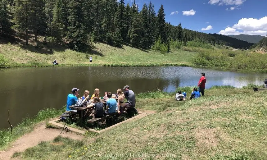 a family at a picnic table by a mountain lake, ready to dig into some of the best hiking snacks 