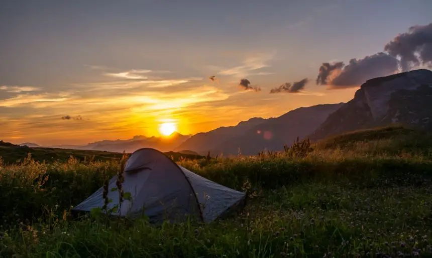 a tent set up with a sunset and mountain view, showing one of the different types of camping