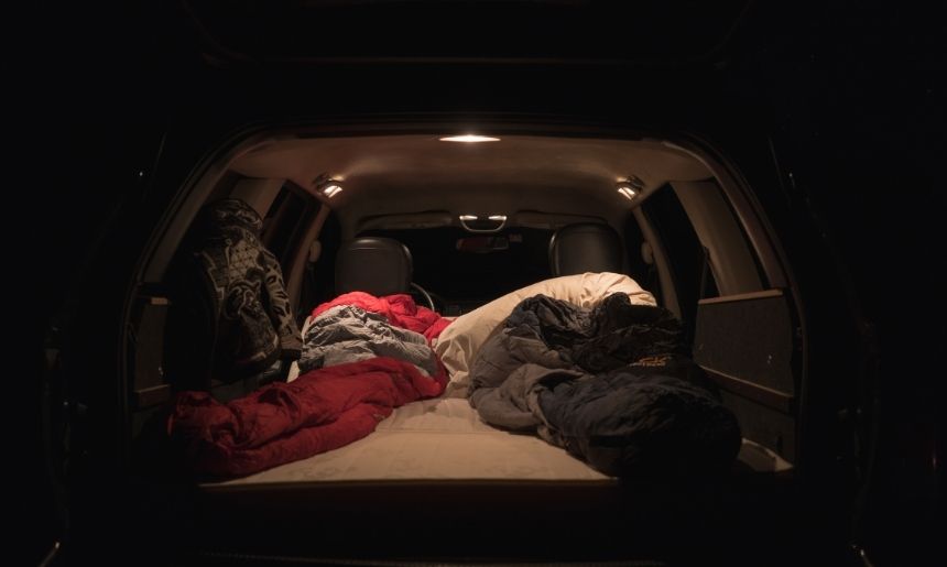 the back of an SUV in the dark, with a sleeping bag laid out to show one of the different camping styles