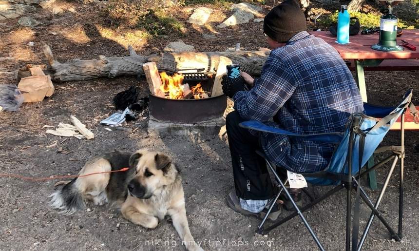 a dog and a man next to a campfire showing how to keep your dog warm while camping
