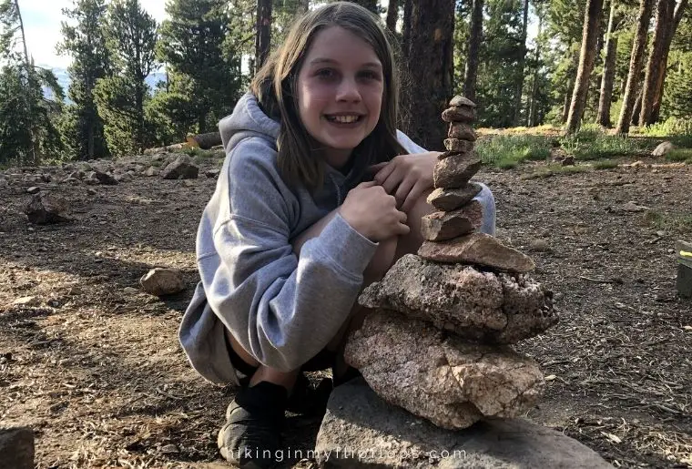 a girl posing next to stacked rocks at a campsite