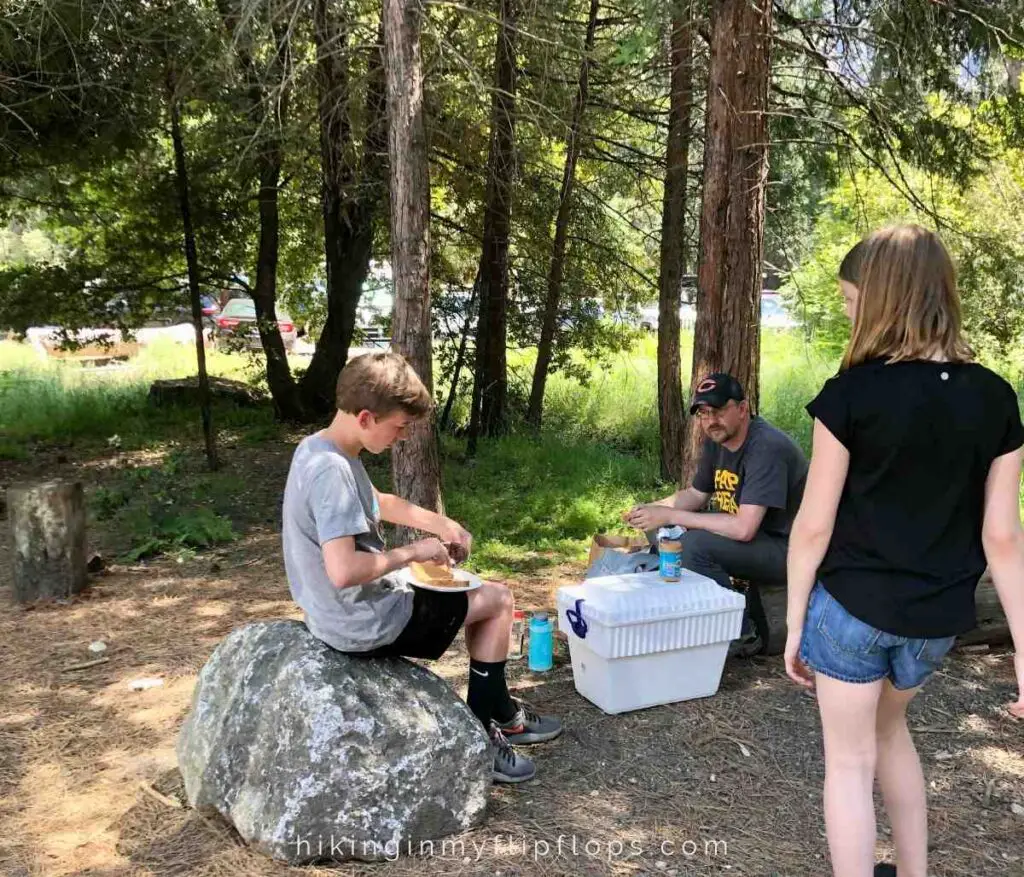 a family sitting on rocks in a wooded area having one of their road trip meals