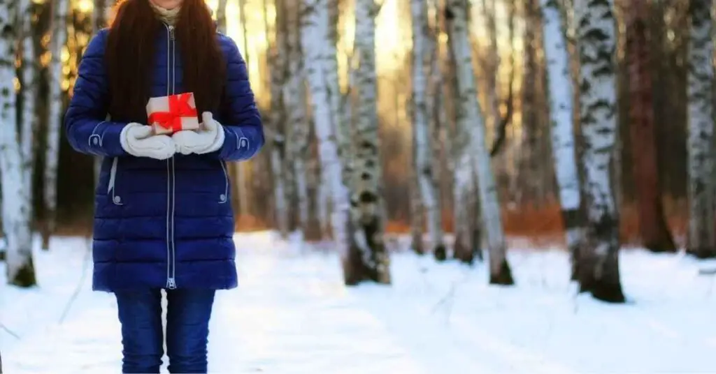 a woman in a snowy forest holding a wrapped present, representing the best gifts for outdoor lovers