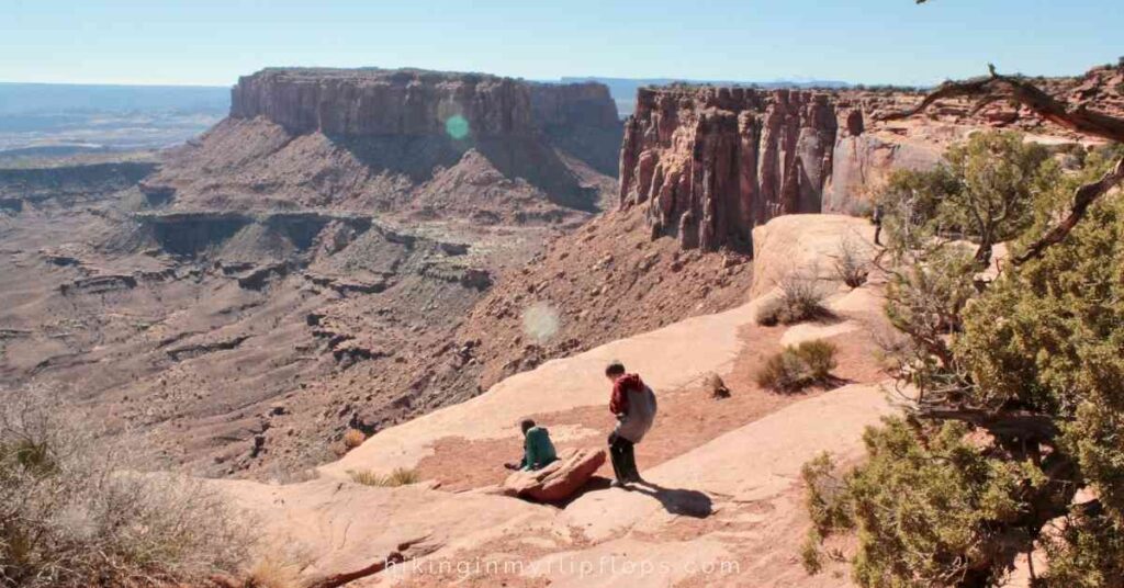 kids sitting on the rocky red terrain to take in views at Canyonlands NP
