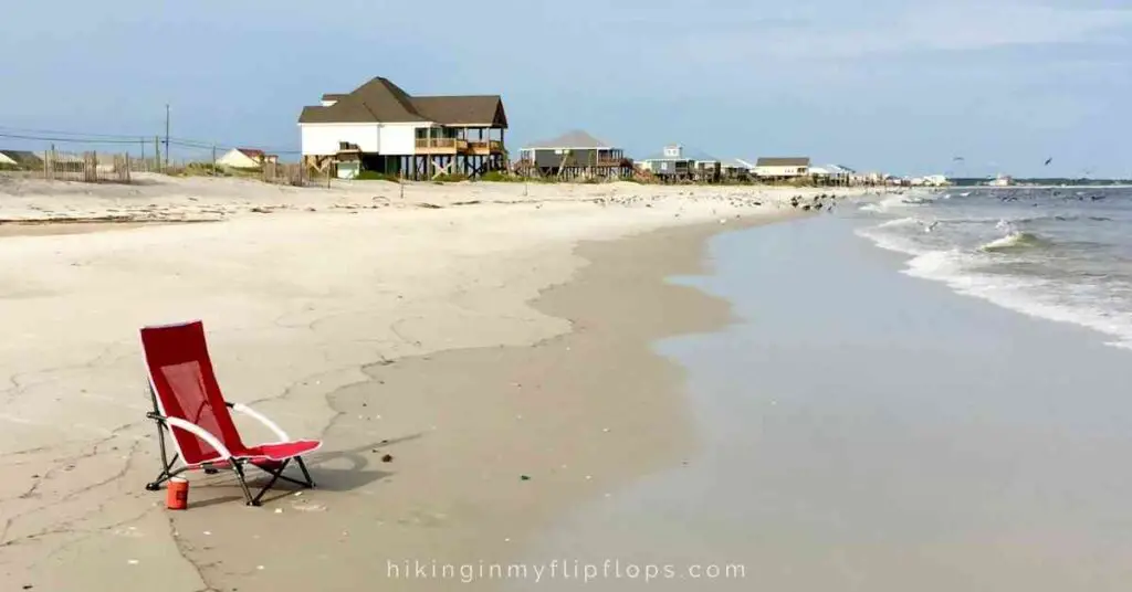 a red beach chair near the water's edge with a row of beach houses in the background