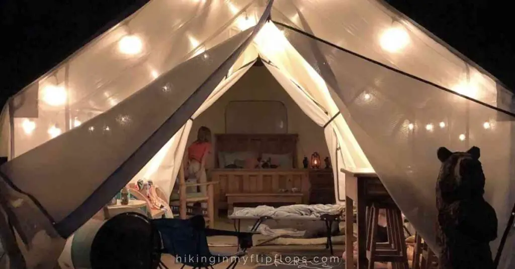 a glamping tent lit up with string lights, fully furnished inside
