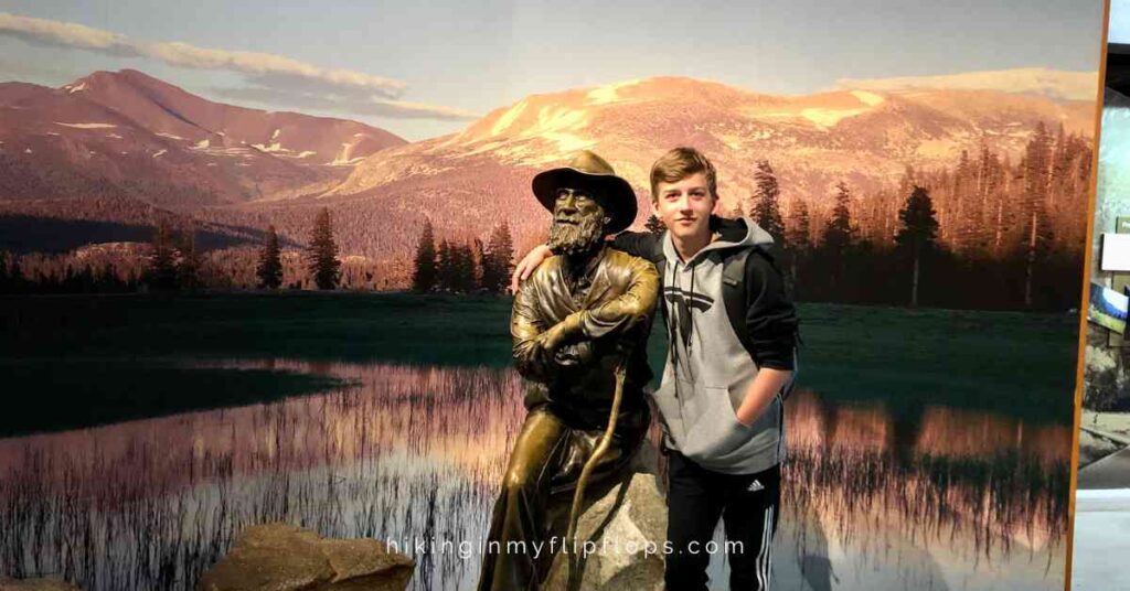 a boy posing with a statue of John Muir when spending a day in Yosemite NP
