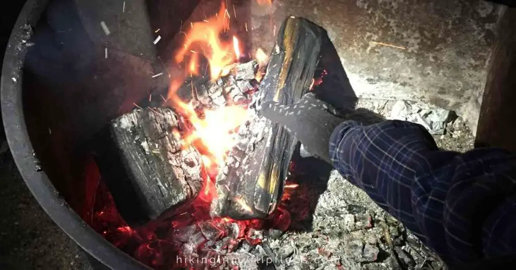 a hand protected with one of the best gloves for campfire cooking reaching into the hot logs