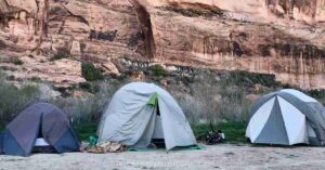 three camping tents set up in front of a canyon wall