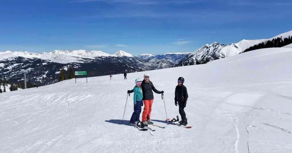 a mom and kids posing for a picture at the top of a ski run depicting a family ski trip packing list